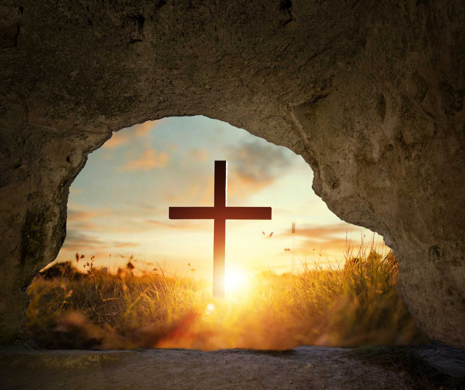 ein großes Kreuz vor einer Hhle stehend. der Blick geht von innen nach draußen. Ein Sonnenunter- oder Aufgang ist zu sehen