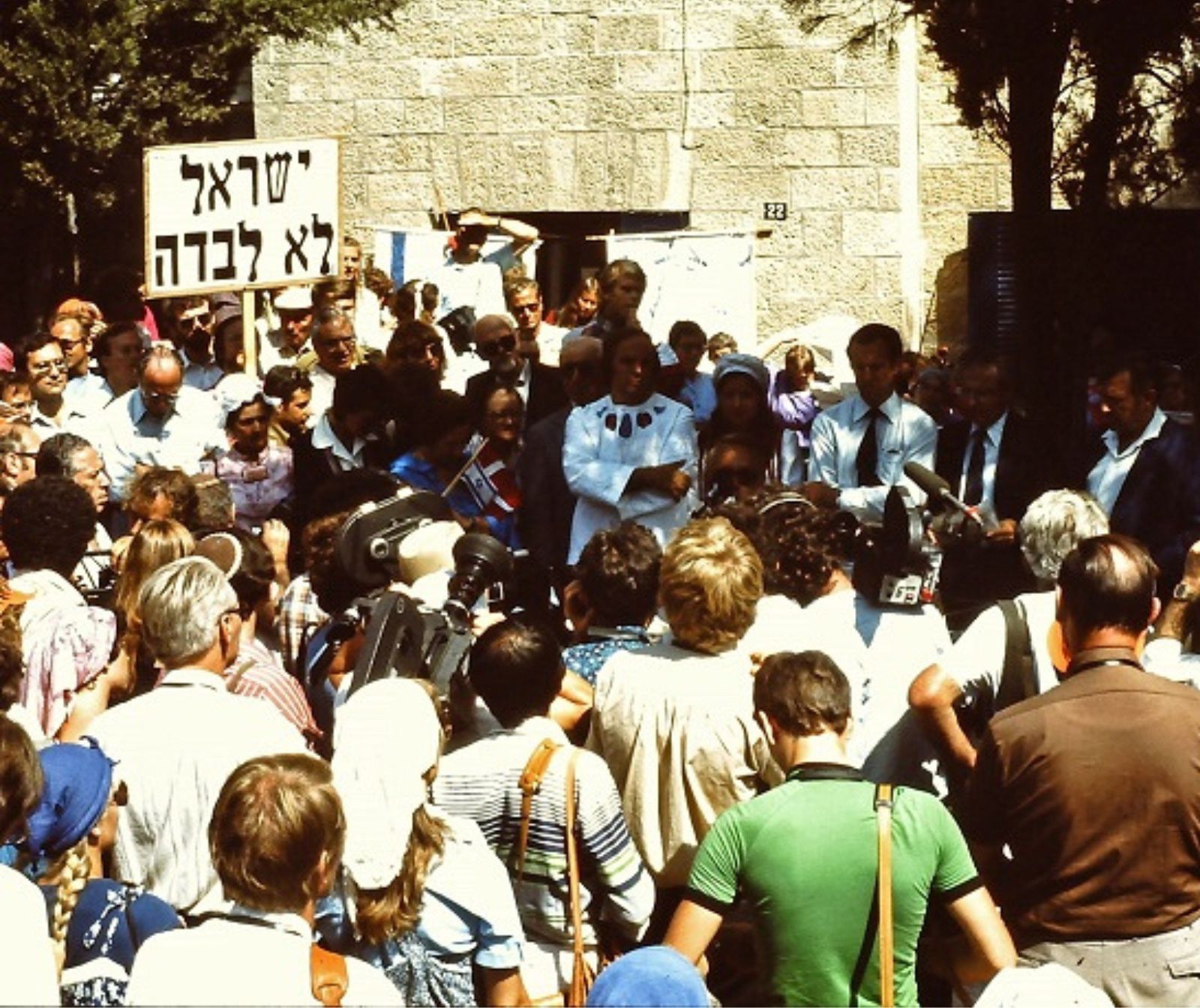 eine ältere Aufnahme von einer Menschenmenge vor einer Steinmauer. Ein Schild mit arabischer Aufschrift ist im Hintergrung