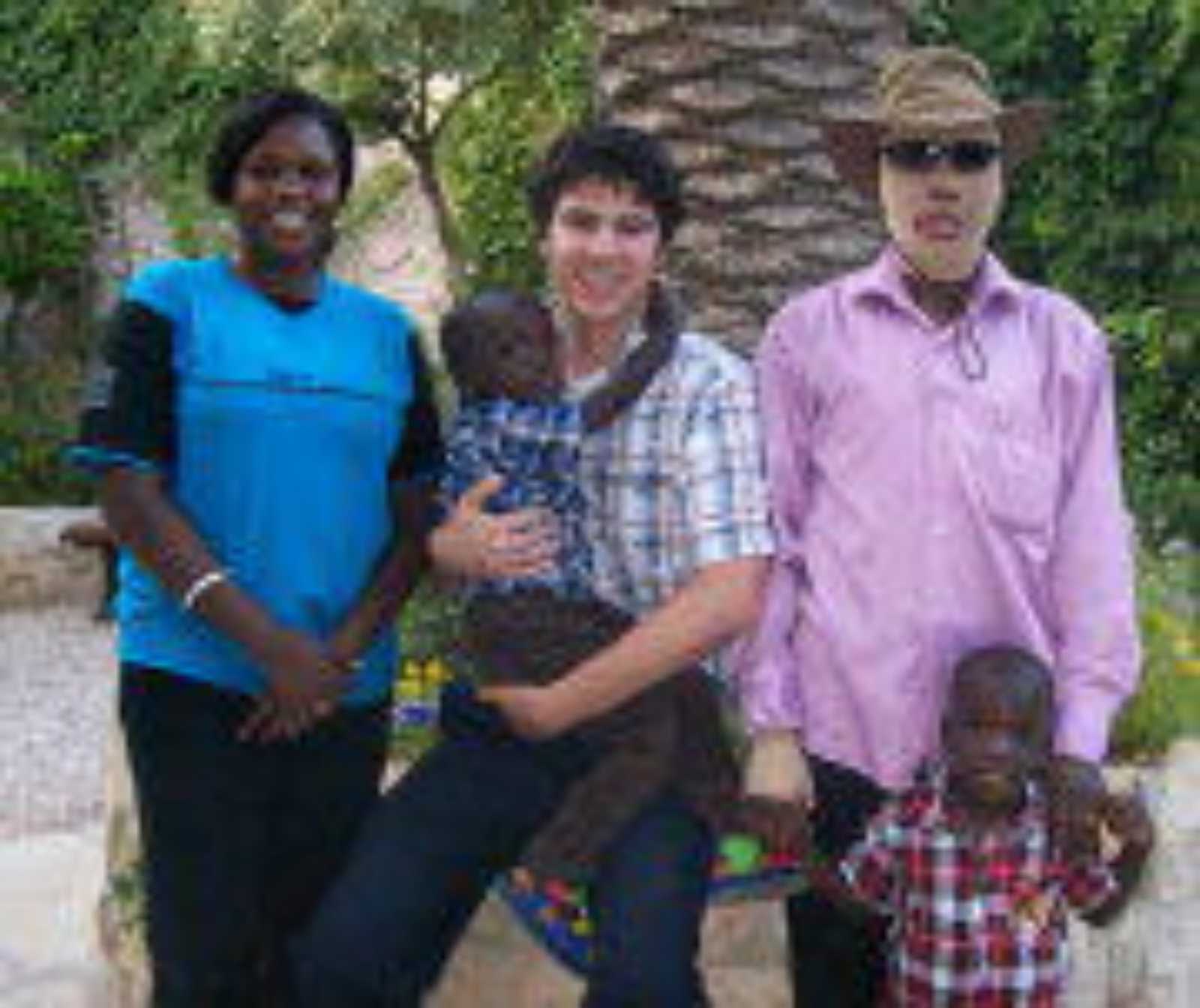 drei Personen nebeneinander. Die Frau in der Mitte hält ein kleines Kind auf dem Arm, der Mann mit eingebundenem Gesicht links neben ihr legt seine Hand auf die schulter eines Jungen, der vor ihm steht