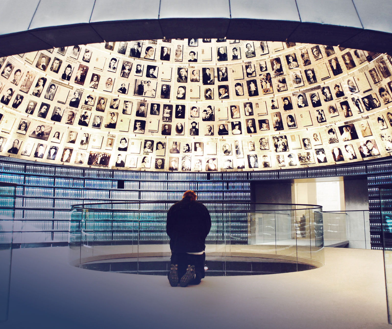 Ein Mann kniet in einem Gebäude unter einer beleuchteten Kuppel, die ausgekleidet mit Fotos von Menschen ist