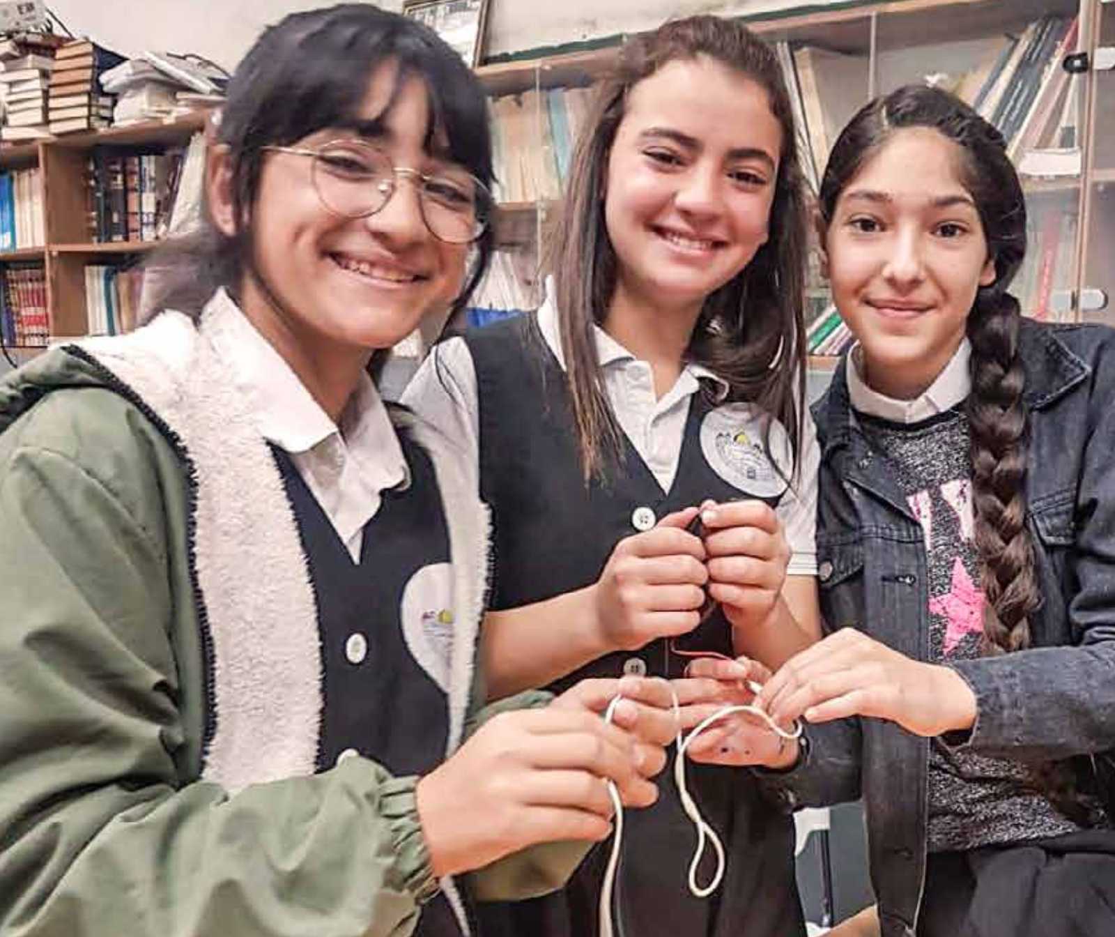 Drei jugendliche mädchen lächeln, sie halten ein weißes Kabel in der Hand