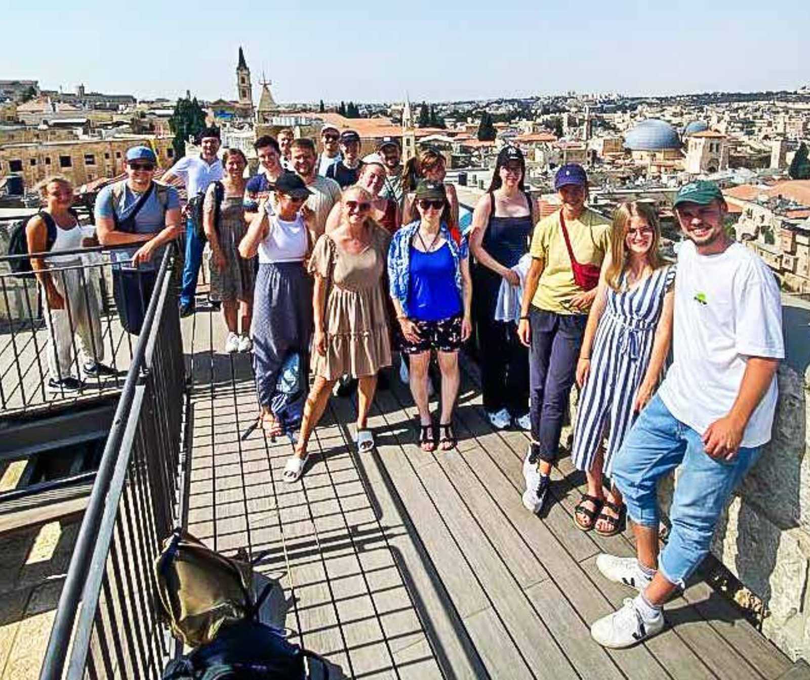 eine Gruppe von junger Menschen steht auf einer APlattform mit Aussicht auf eine Stadt. Es sind neben den Wohnhäusern Kirchtürme, Türme und Kuppeln zu sehen.