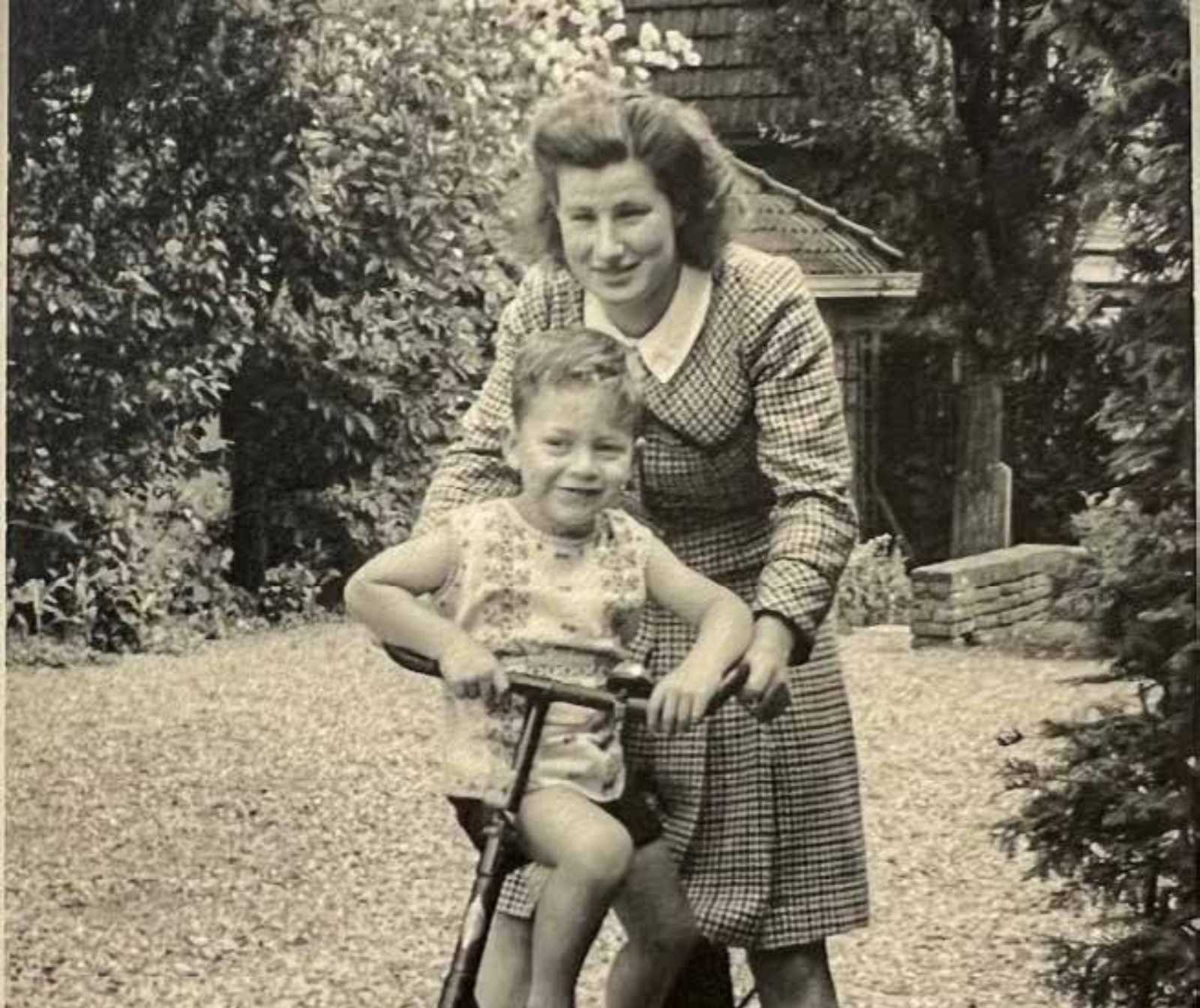 eine altes schwarz/weiß Foto. Ein Frau hält einen kleinen Jungen von hinten auf einem Fahrrad fest