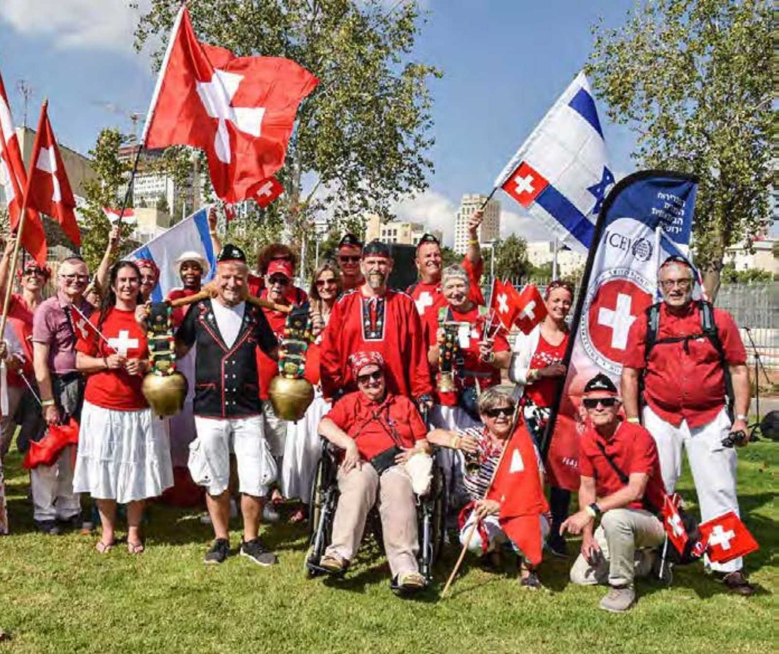 eine Gruppe von Menschen in rot weißer Schweizer Trachten oder Alltagskleidung posieren für ein Gruppemfoto. Mehrere Schweizer Flaggen sind zu sehen