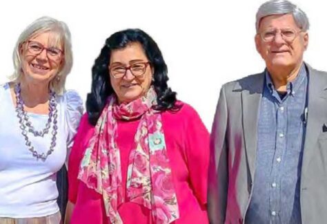 Zwei Frauen ein Mann stehen nebeneinander, sie lächeln. Es scheint die Sonne.