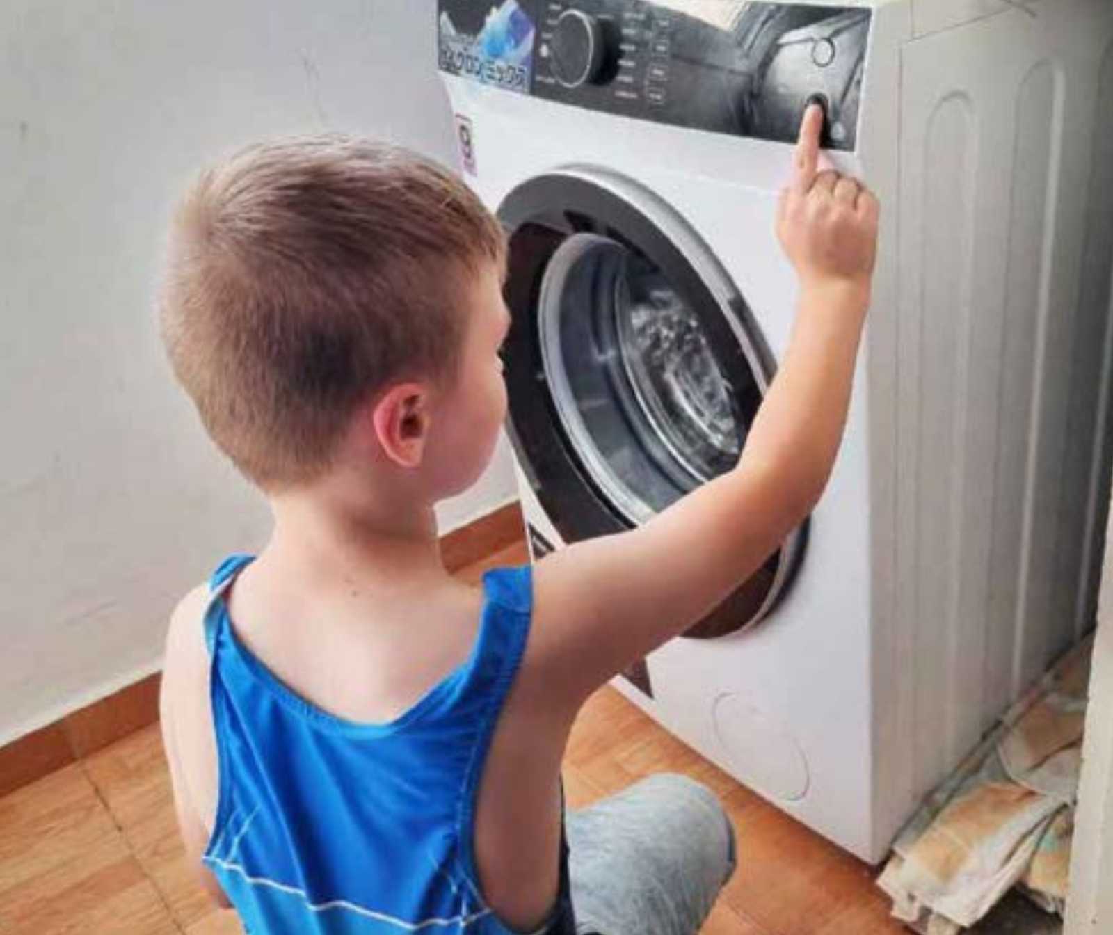ein kleiner Junge in der Hocke vor einer Waschmaschine, die er gerade betätigt