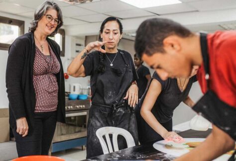 Zwei Frauen sthen vor einem Tisch, an dem ein junger Mann und eine junge Frau kozentriert arbeiten. Auf dem Tisch liegt eine Teigrolle und eine Rührschüssel