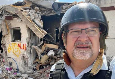 Ein Mann mit Helm steht vor einem Wohnhaus, das in Trümmern liegt