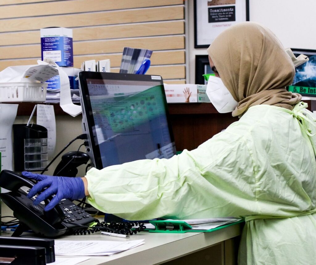 Integration und Aufstieg: Arabische Israelis erobern das Gesundheitswesen - Eine Frau mit braunem Kopftuch, Atemschutzmaske, blauen Handschuhen und grünem Kittel steht vor einem Computer in einem Krankenhaus.