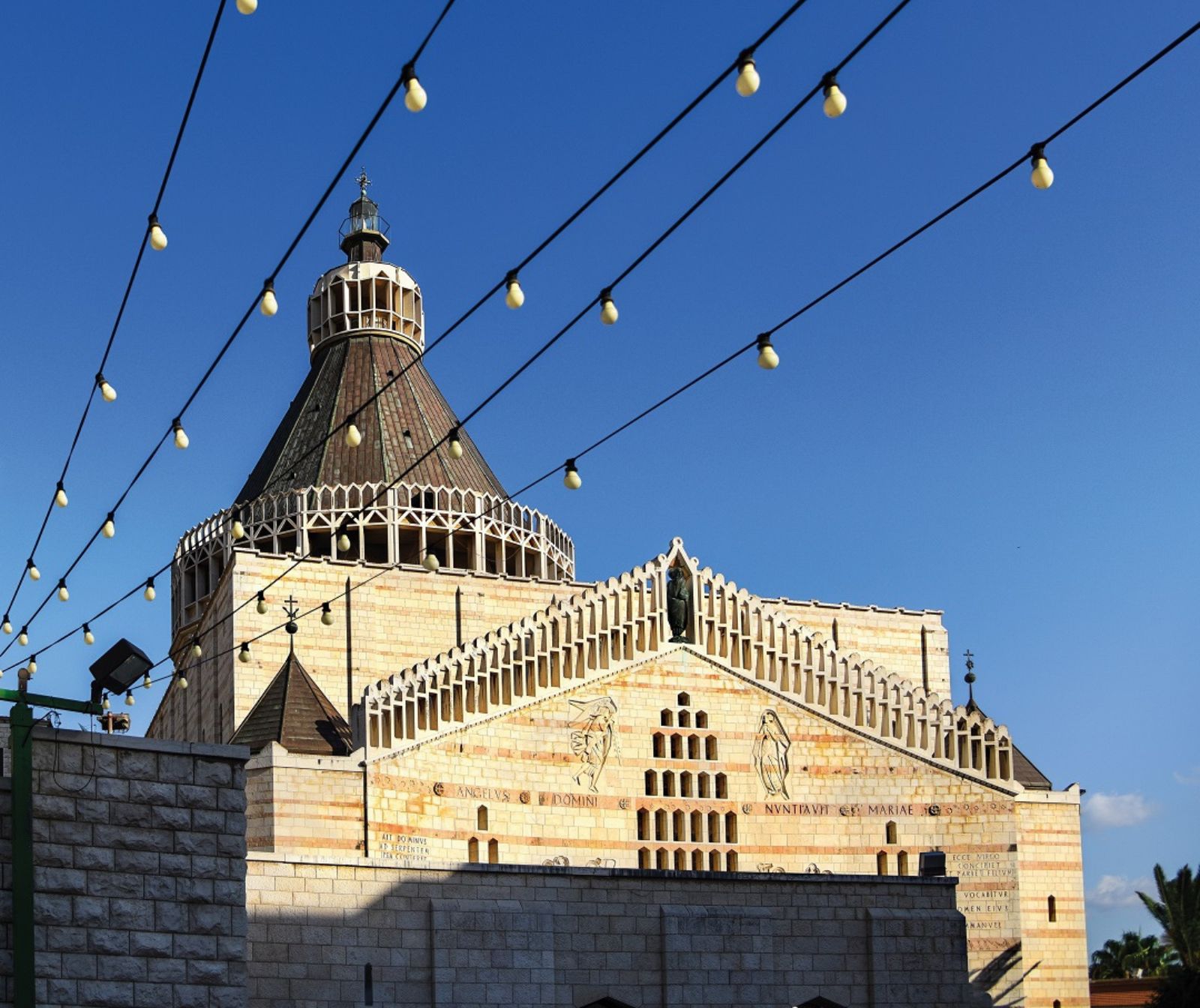 Die Sonne kommt von vorne und beleuchtet sandfarbene Steine, dekorativ gemeißelte Steinverziehrungen, Heiligenfiguren, zwei kleine und einen großen Turm mit braunen Dachziegeln.