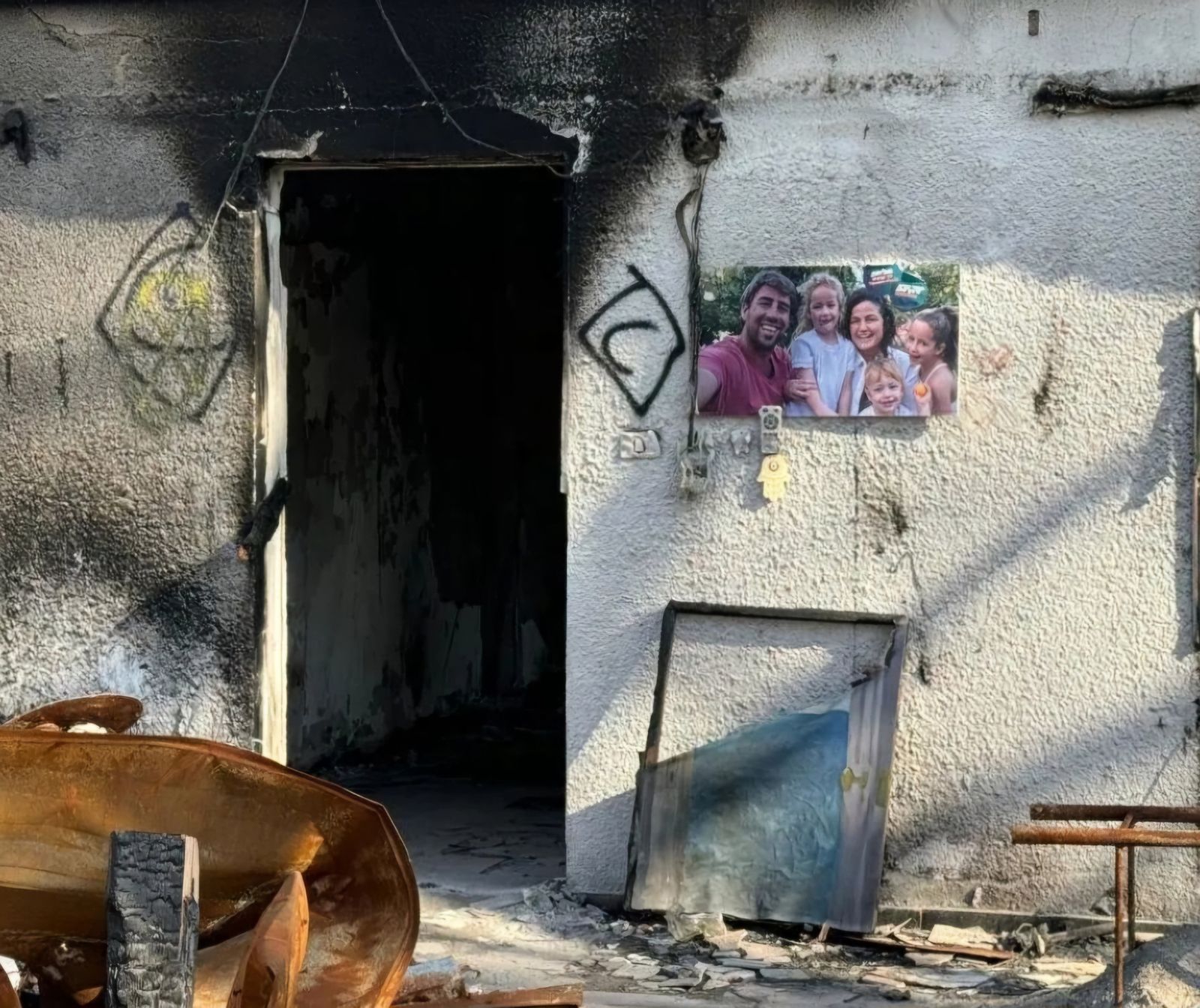 Feuergeschwärzte Wände, kaputtes Glas und Einschusslöcher am Eingang zu einem Haus in einem israelischen Kibbuz. Hier lebte eine fünfköpfige Familie mit kleinen Kindern, bevor sie von der Hamas ermordet wurden. Ein Foto der Familie hängt neben dem Hauseingang.