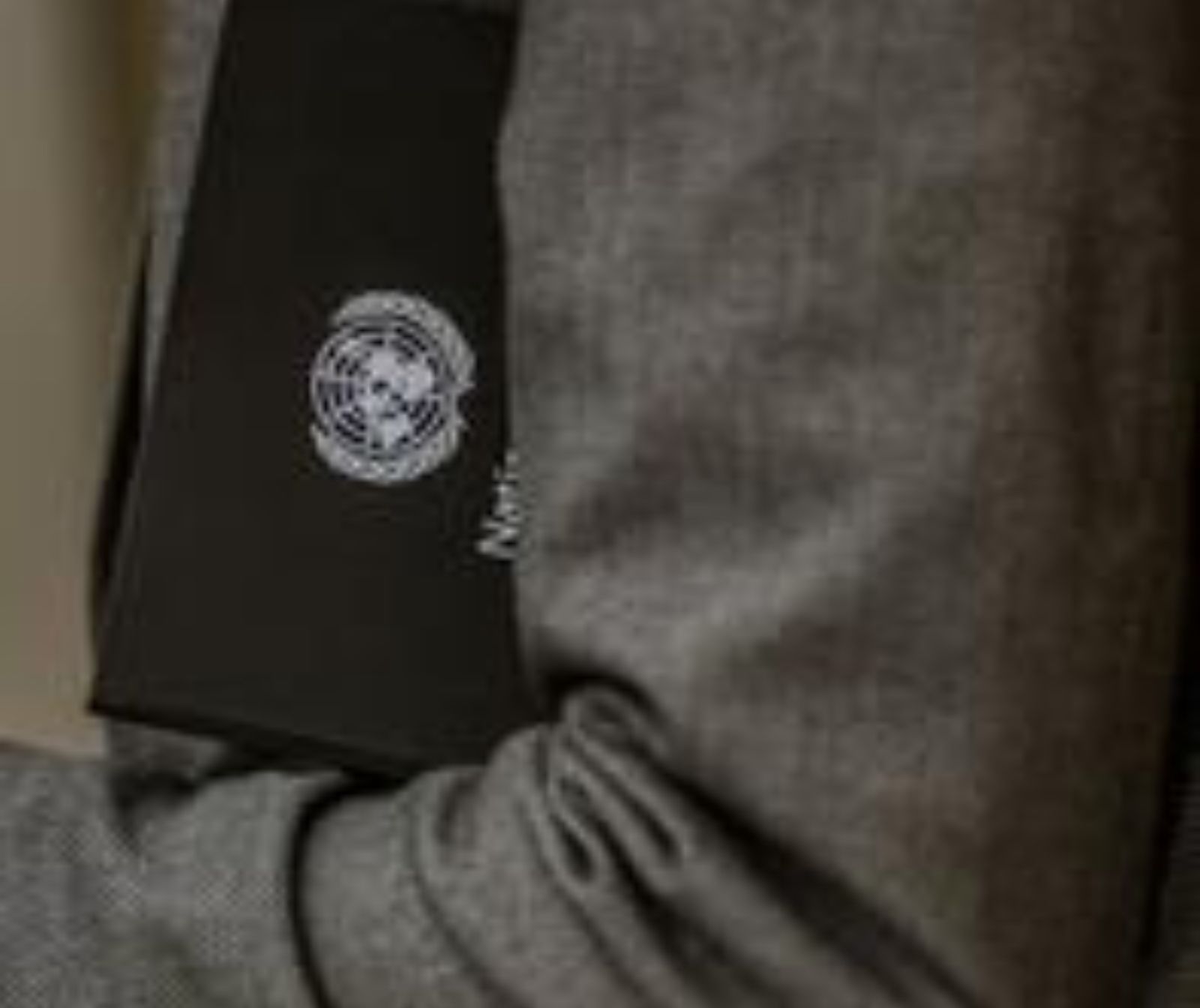 Applikation der UNRWA auf einer schwarzen Mappe, welche unter einem Arm eingeklemmt ist. Der Mann trägt ein graues Jackett