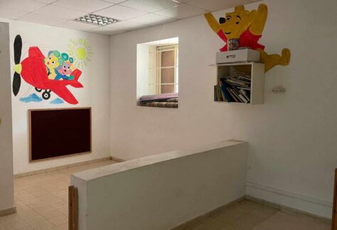 ein leerer raum mit kindlichen Wandzeichnungen und einem kleinen Wandregal mit Heftchen