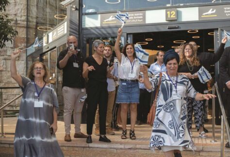 eine Gruppe von menschen auf einer Treppe vor einer Flughafenhalle. Sie winken mit Israel Fähnchen in der Hand