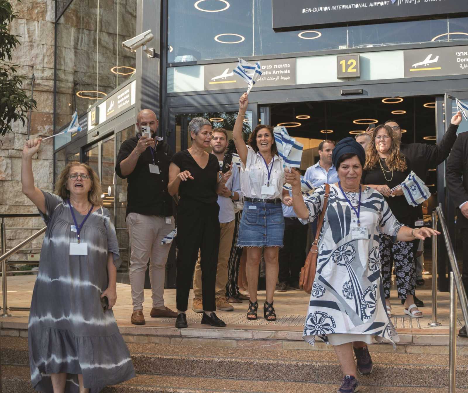 eine Gruppe von menschen auf einer Treppe vor einer Flughafenhalle. Sie winken mit Israel Fähnchen in der Hand