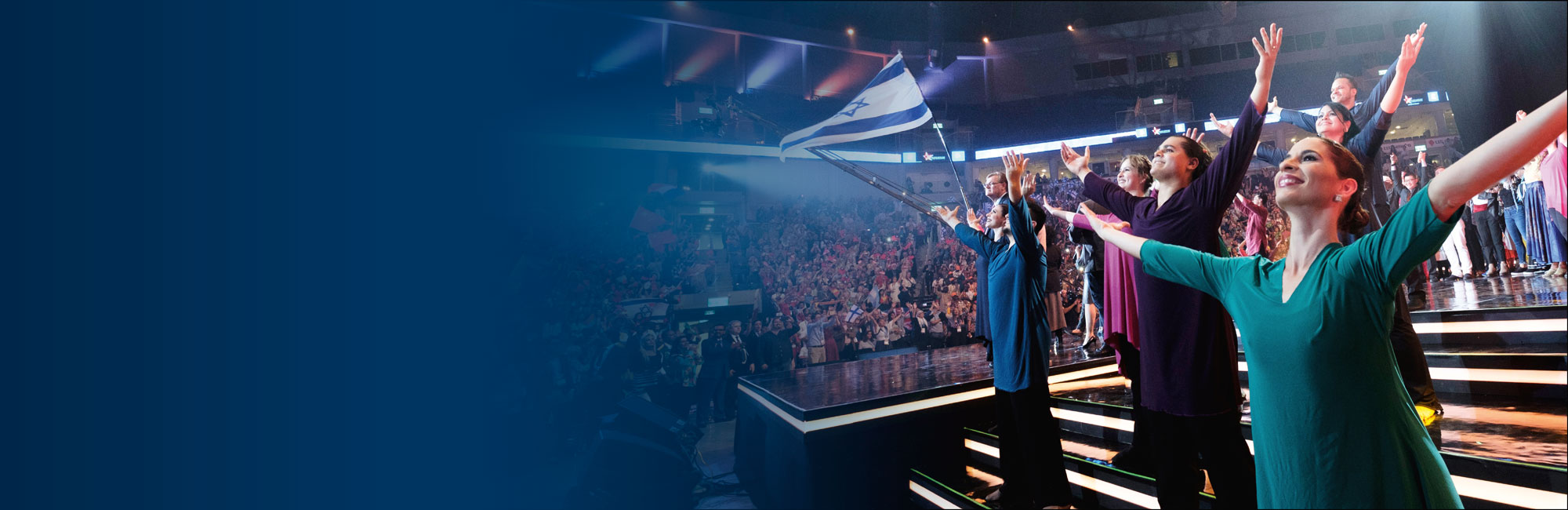Tänzer haben erhobene Hände und stehen auf einer Bühne in vollem Saal