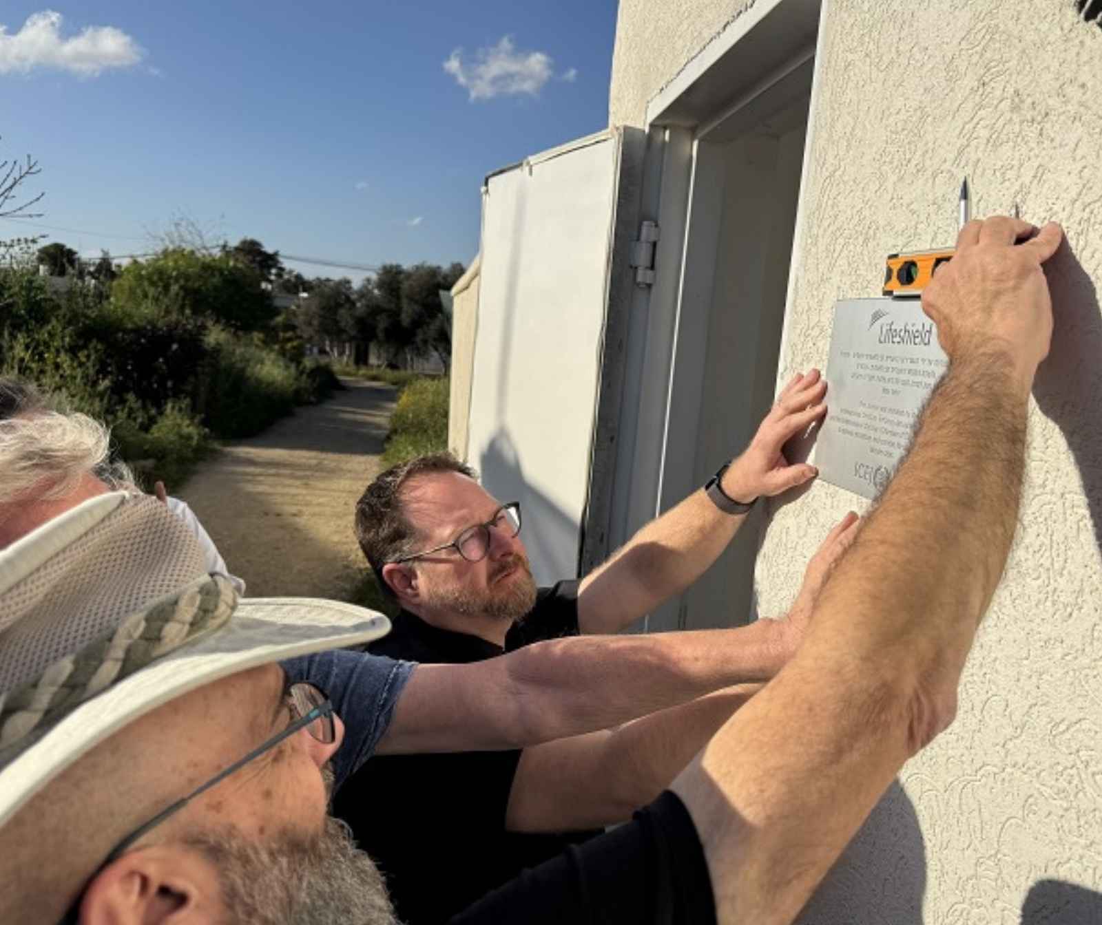 drei Männer bringen ein schild an einer Außenwand eines Gebäudes an