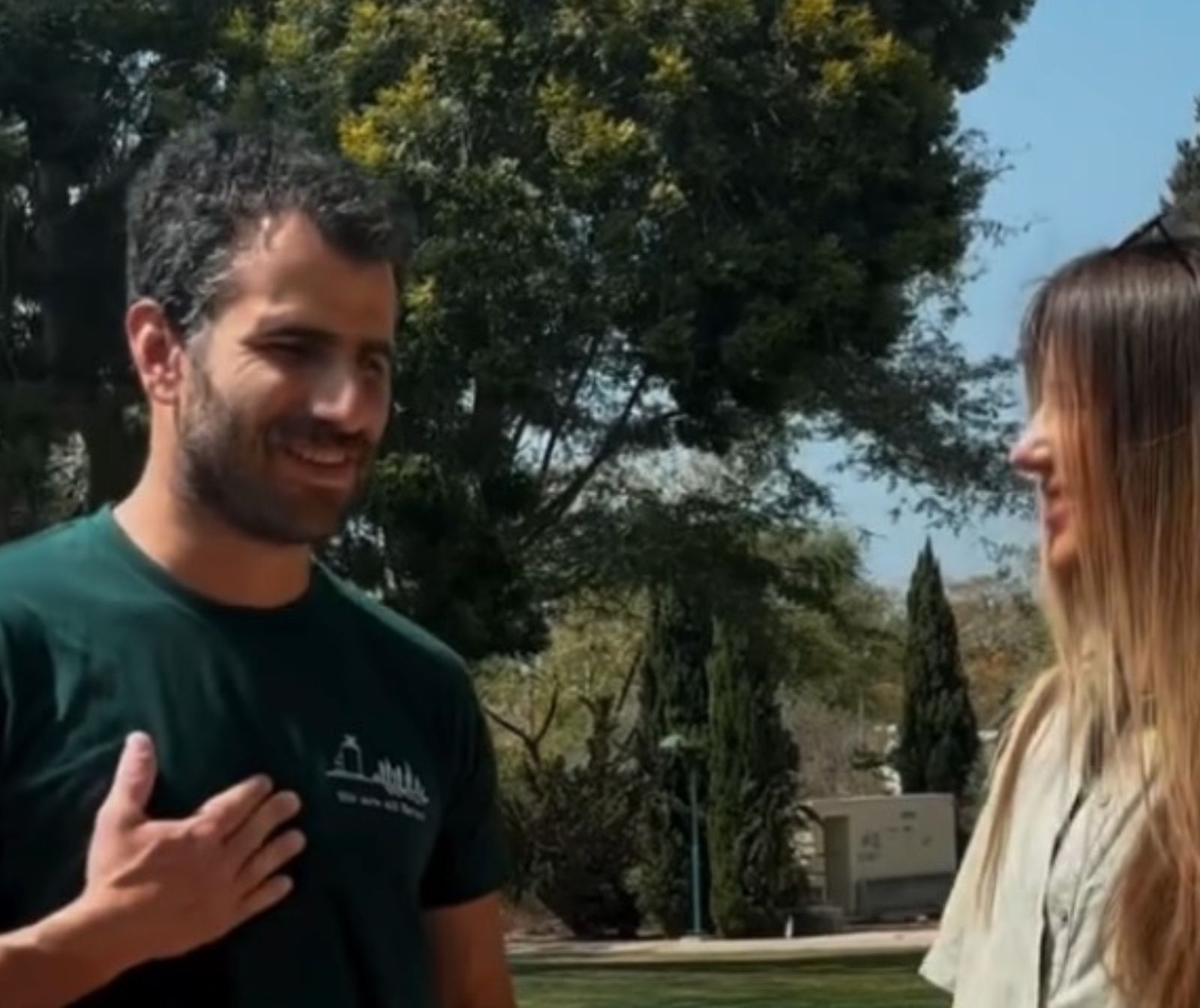 ein jüngerer Mann und eine jüngere Frau unterhalten sich draußen, es scheint die Sonne