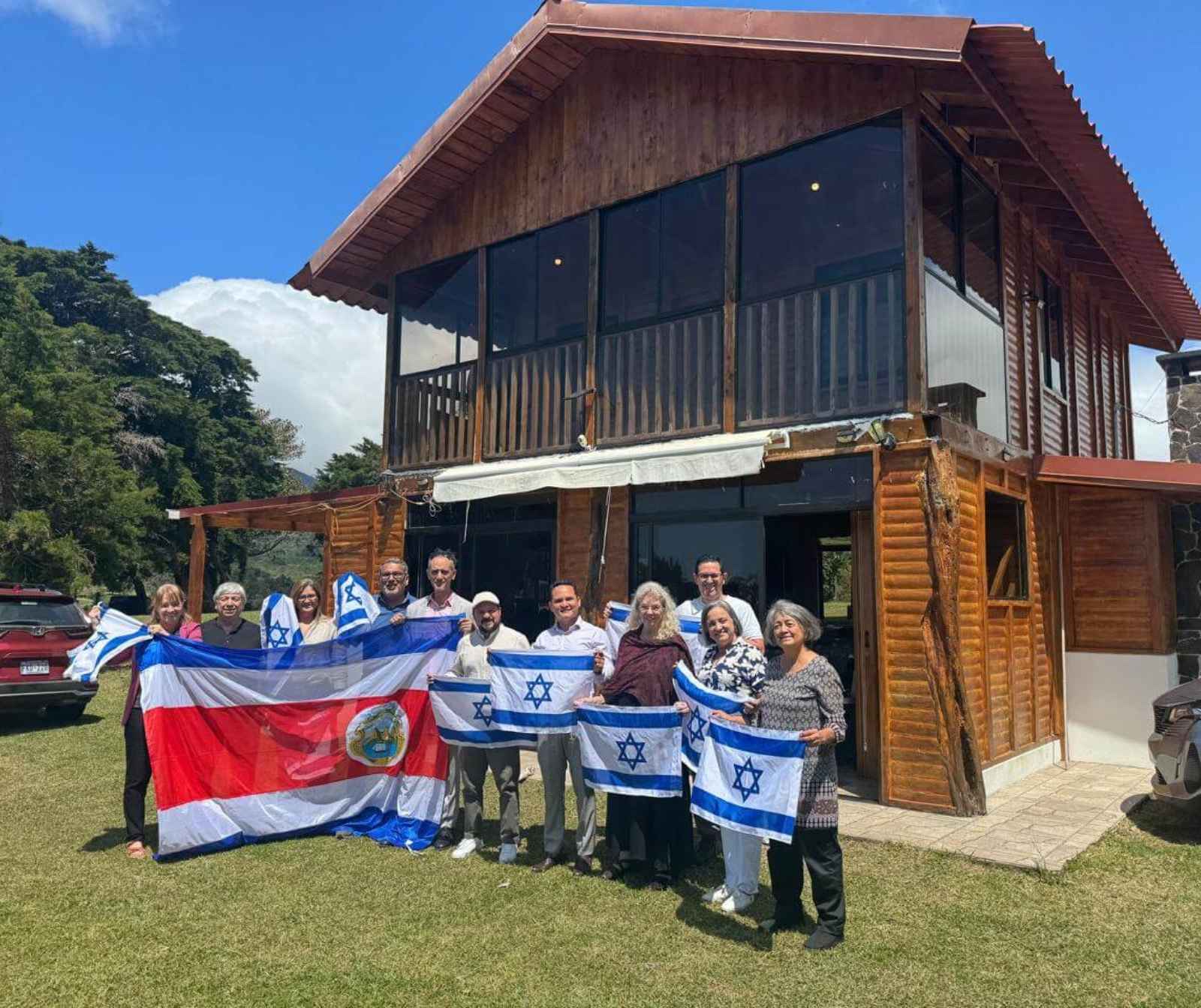 eine Gruppe von Menschen mi Israel Fahnen und der Costa Rica Flagge vor einem Holzhaus
