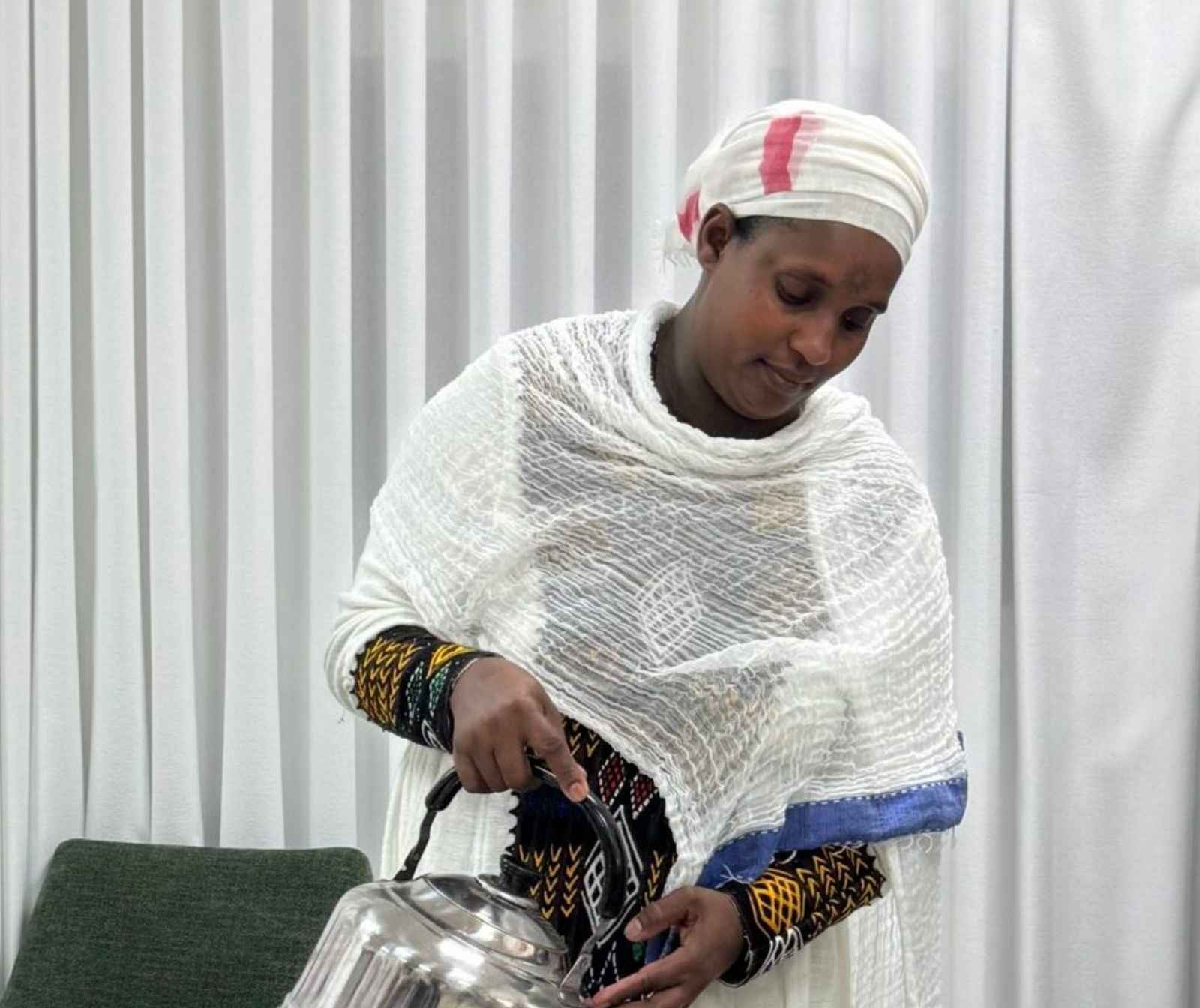 eine dunkelhäutige Frau in landestypischem Outfit hält eine silberfarbene Kanne in der Hand