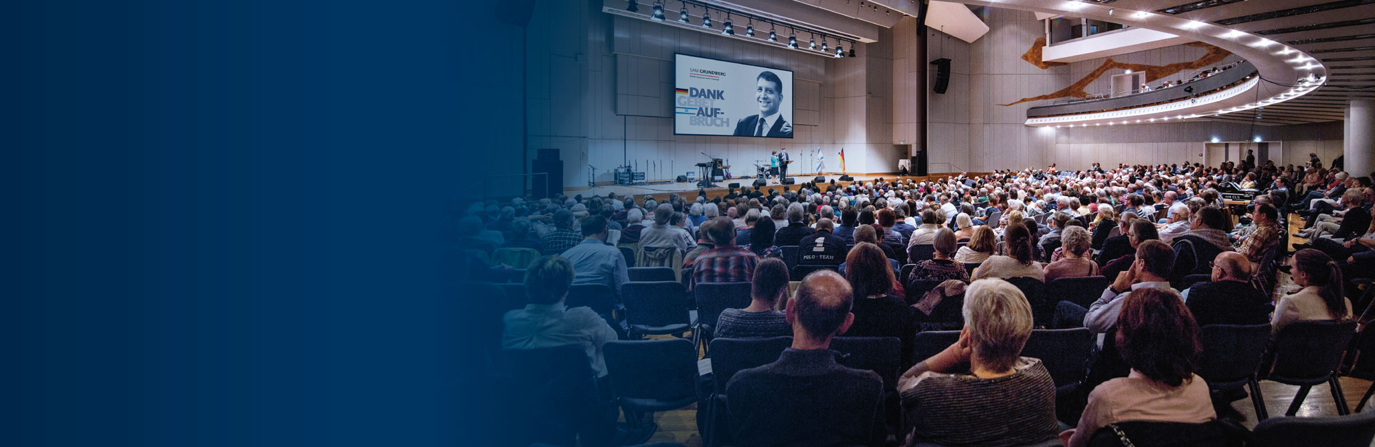 Großer Saal mit zuschauern und Sprechern auf der Bühne