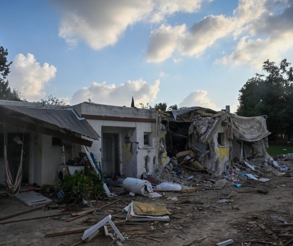 Ein zerstörtes Haus in Kibbuz Kfar Aza. Die Wände sind übersäht mit Einschusslöchern. Fenster und Türen zerschlagen. Vor dem Haus liegen zerstörte Möbelstücke. Das Hausdach ist eingefallen.