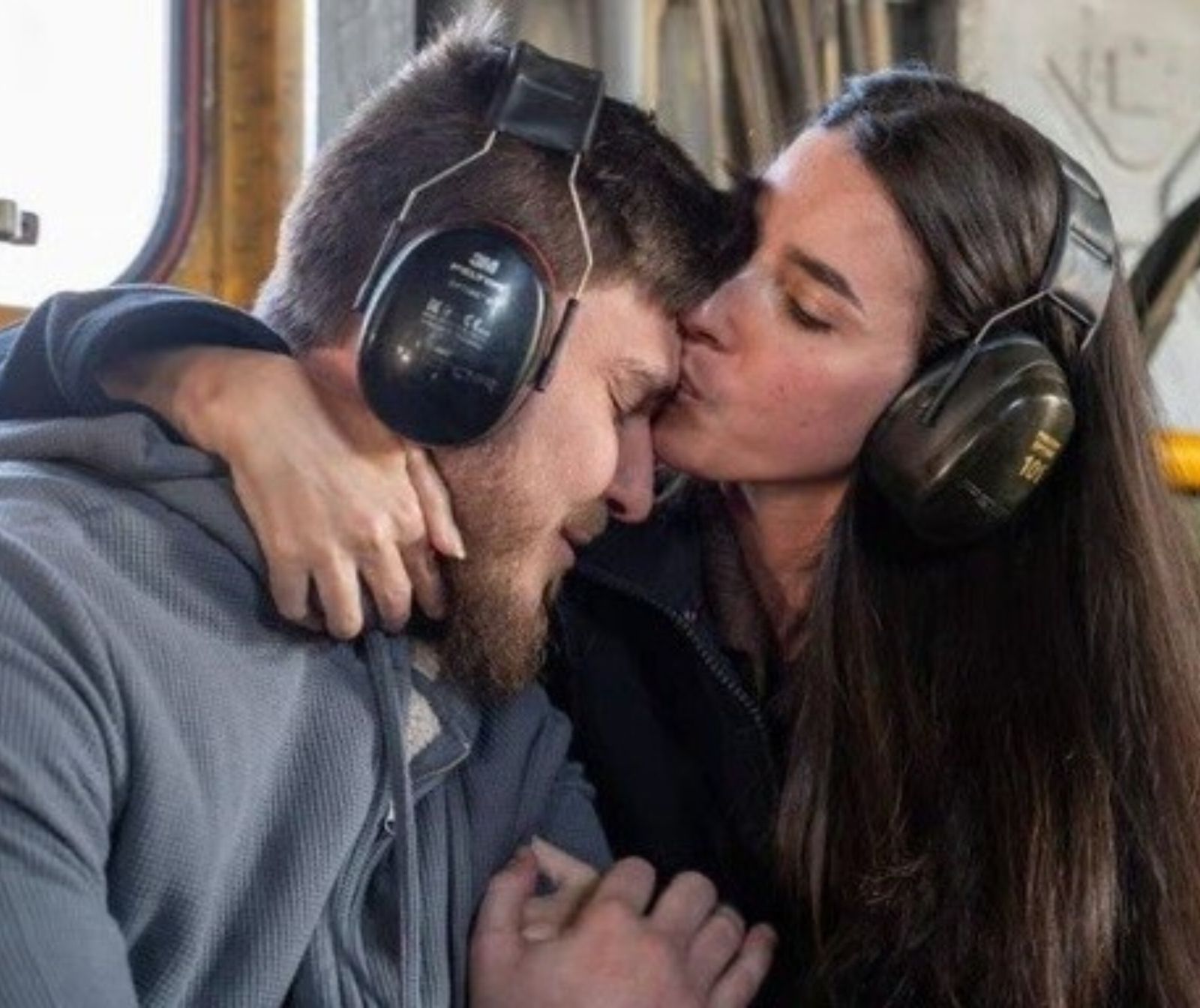 Links im Bild ein Mann im grauen Pullover, rechts eine Frau. Er hält ihre Hand, sie hat ihre andere Hand um seine Schultern gelegt und küsst ihn auf die Stirn.
