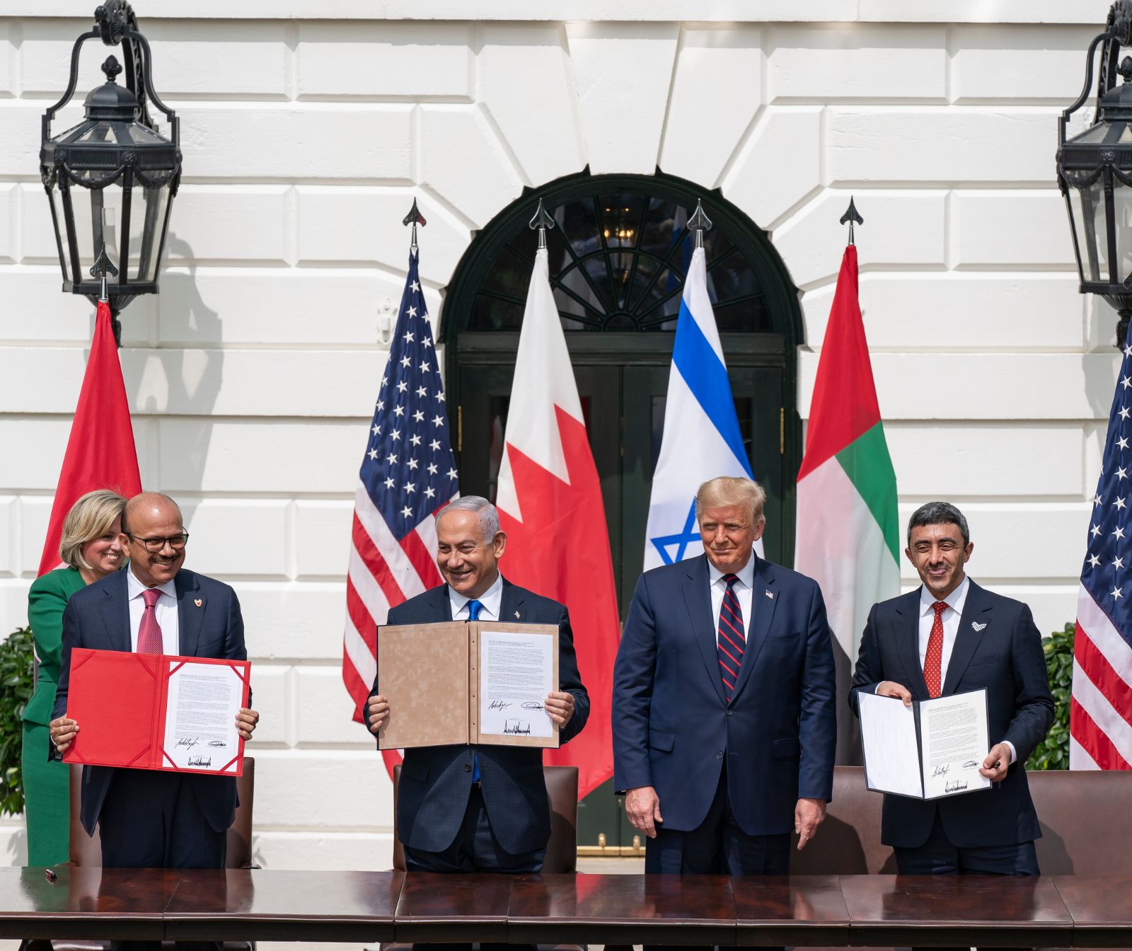 V.l.n.r. stehen der Außenminister Bahrains, Ministerpräsident Netanjahu, Präsident Trump und der Außenminister der Vereinigten Arabischen Emirate. Sie stehen hinter einem Tisch und halten die unterschriebenen Abkommen in die Kamera.