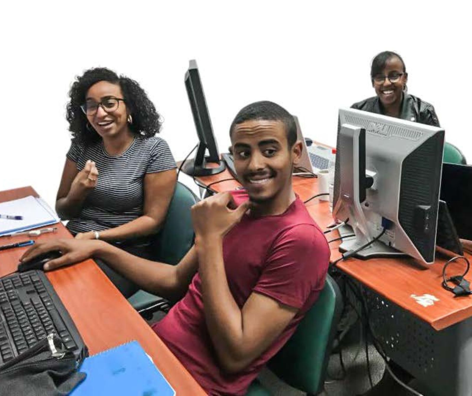 junge Menschen sitzen an ihren PCs an zwei Tischen und lächeln. Sie haben dunkle Hautfarbe