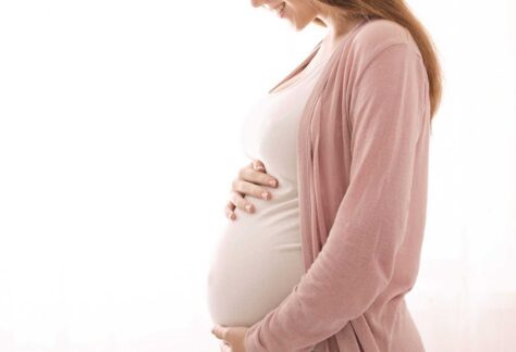 eine schwangere Frau, die ihren runden Babybauch liebevoll mit ihren beiden Händen umschließt