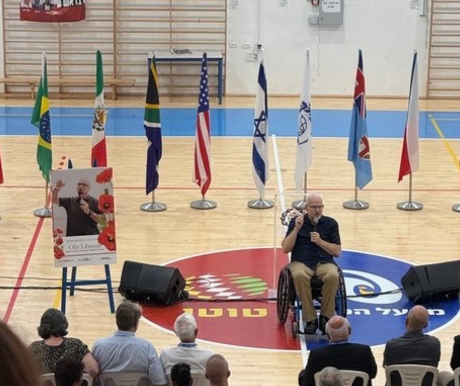 Erfülltes Versprechen - ein Mann im Rollstuhl spricht in einer Turnhalle zu Menschen