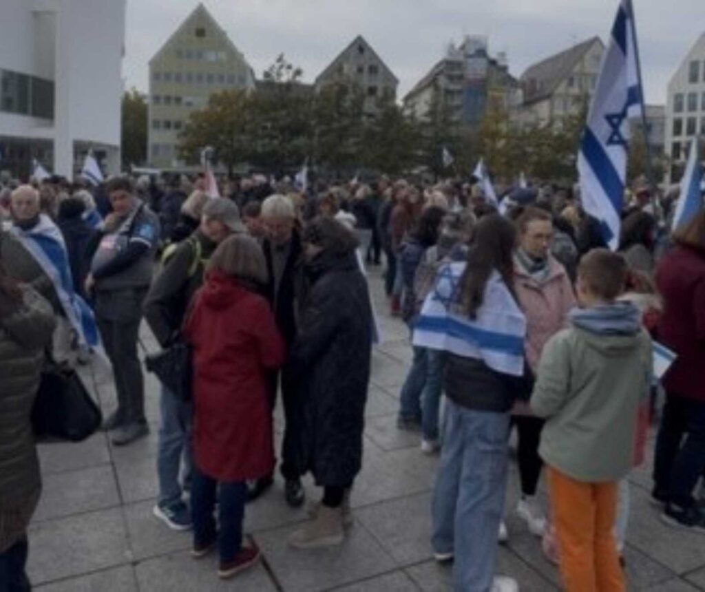 Täglich Drohbriefe und Beleidigungen - Menschen stehen auf einem Platz in Grüppchen zusammen, manche haben eine Israelflagge