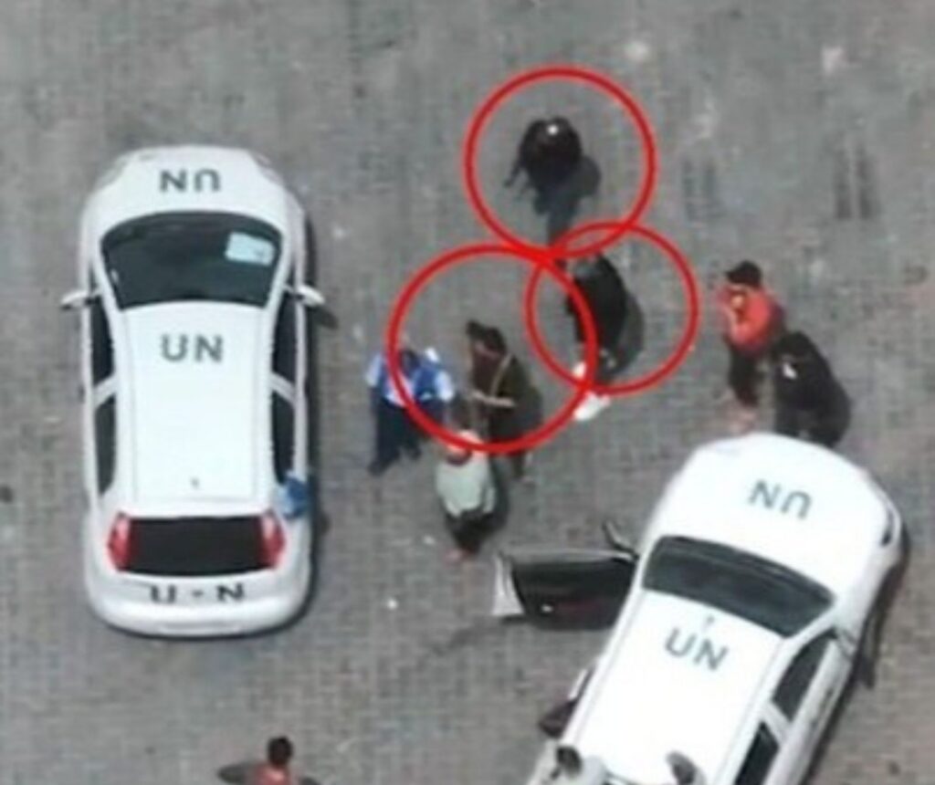 eine Drohnenansicht zweier UN Fahrzeuge. Zwischen ihnen befinden sich mehrere Menschen, drei davon, welche mit roten Kreisen markiert sind, sind bewaffnet