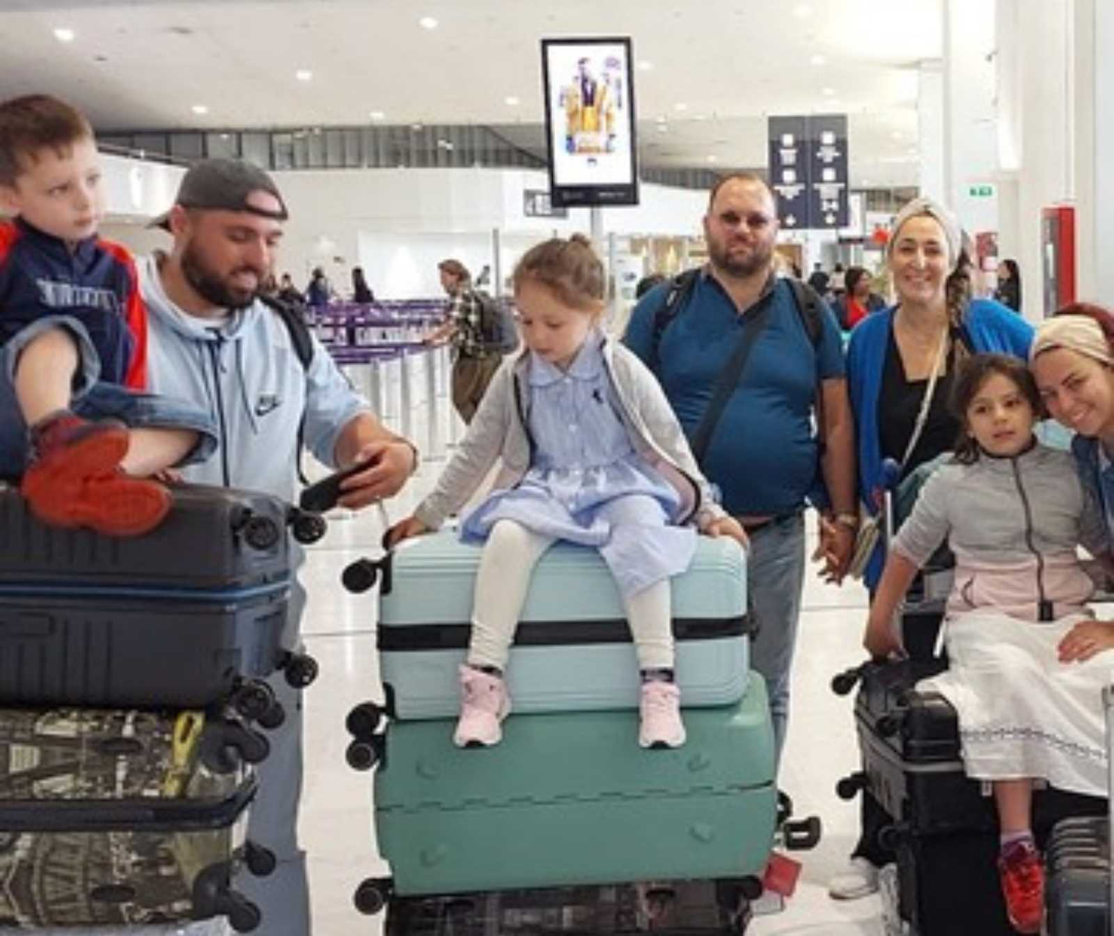 mehrere Familien in einer Hall. Sie fahren wägen mit Stapeln von Koffern, auf denen Kinder sitzen