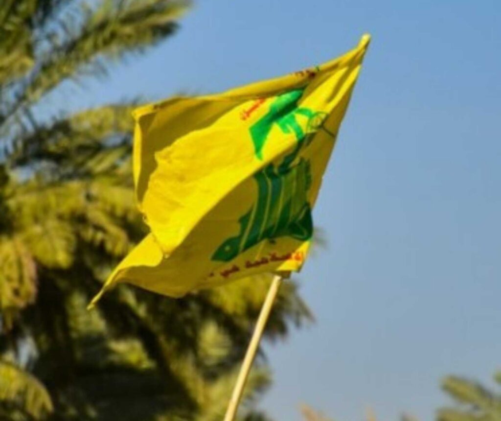 Hintergrund: blauer Himmel und Palmen. Vodergrund: gelb/grüne Fahne der Hisbollah weht