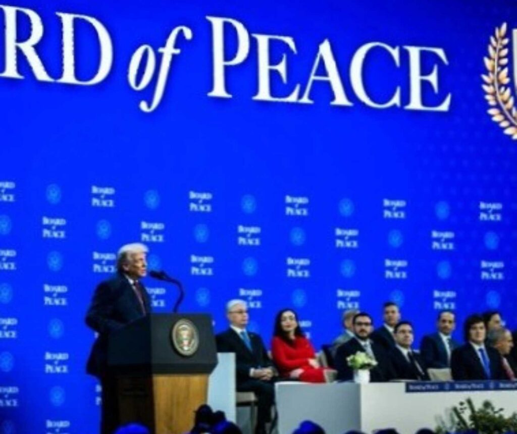 Ein Mann steht vor einer blauen Wand, auf der etwas in Teilen nur zu lesen ist: of Peace. Er spricht in ein Mikfofon am Pult, neben ihm sitzen mehrere Personen an einem langen Tisch