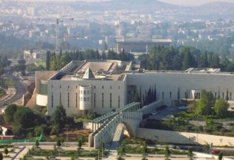 ein großer modernerer Gebäudekomplex mit einer Grünanlage davor. Im Hintergrund sieht man eine Stadt