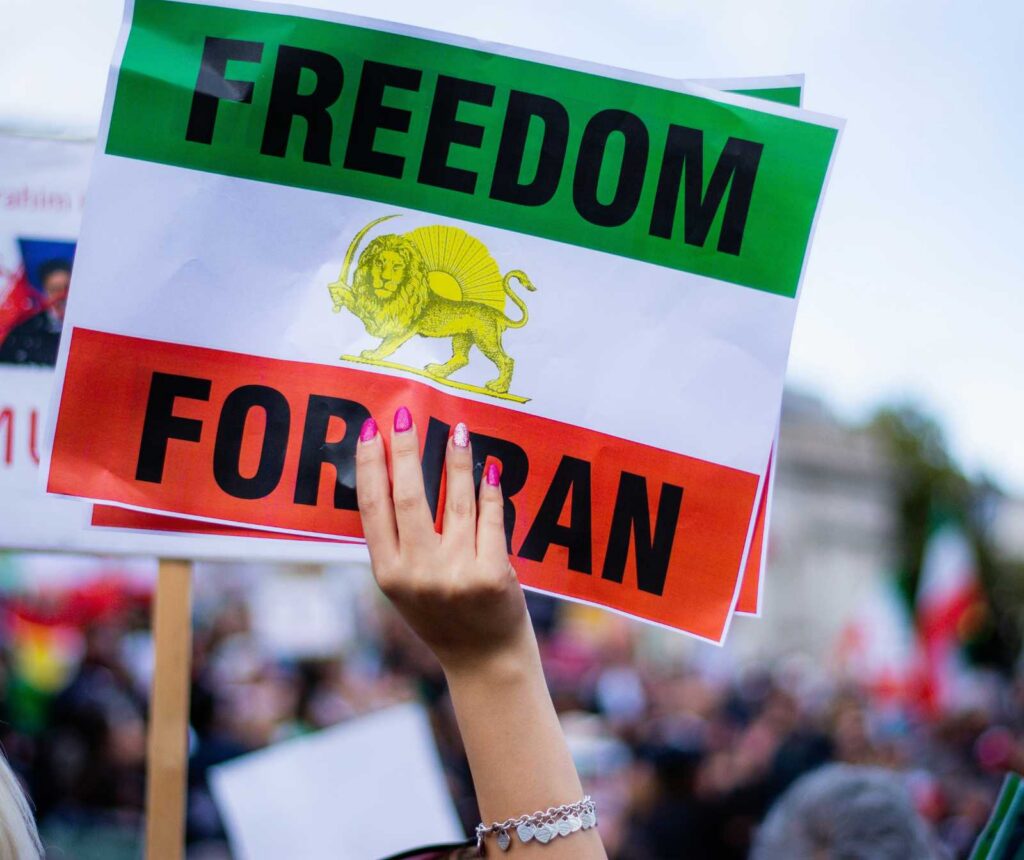 eine Frauenhand mit pinken Fingernägeln hält ein Schild mit iranischer Flagge und der Aufschrift 'Freedom for iran' in die Luft