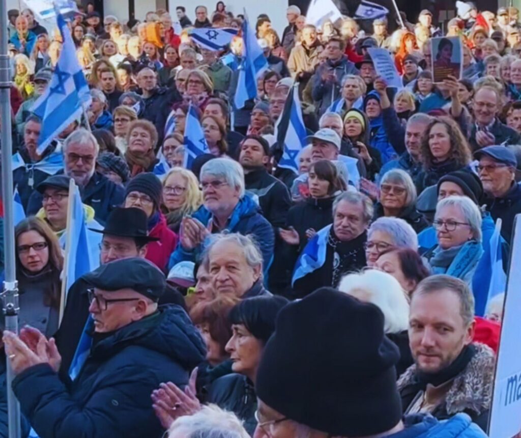 Menschenauflauf auf der Straße. Sie tragen Winterjacken und Israelfahnen