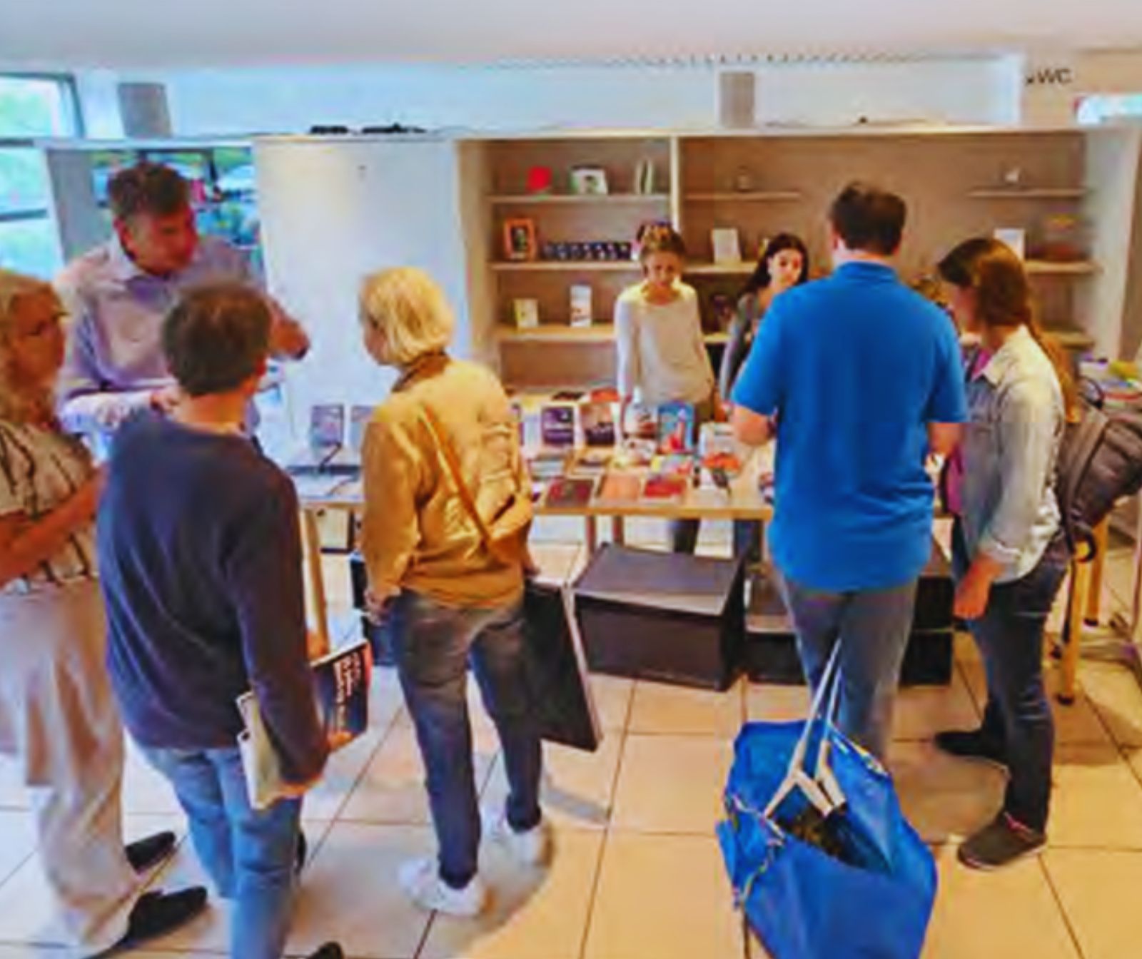 mehrere personen in einem Raum mit Regal und Tischen, in dem bzw. auf denen Bücher etc ausgelegt sind