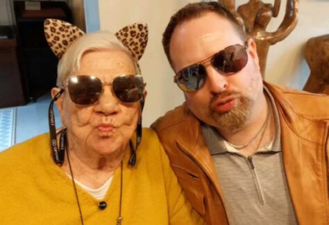 ein ältere Dame und ein Mann, beide mit Sonnenbrille, sie mit Stoff-Leopardenohren auf, machen spielerische Kussmund-Pose