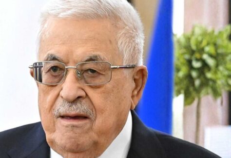 ein älterer Mann mit weißem Haar und Brille. Er trägt einen blauen Anzug, ein weißes Hemd mit blauer Krawatte