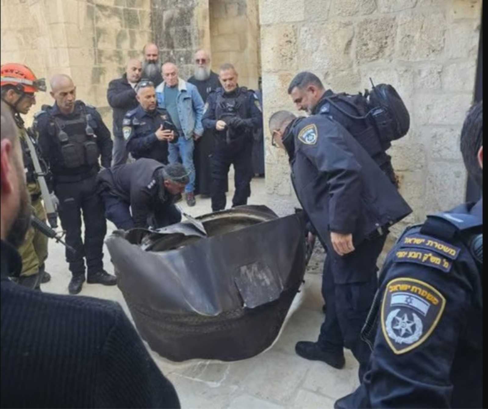 Mehrere Soicherheitskräfte und Einsatzpersonen in einer engen Straße begutachten ein großes beschädigtes Metallteilam Boden.