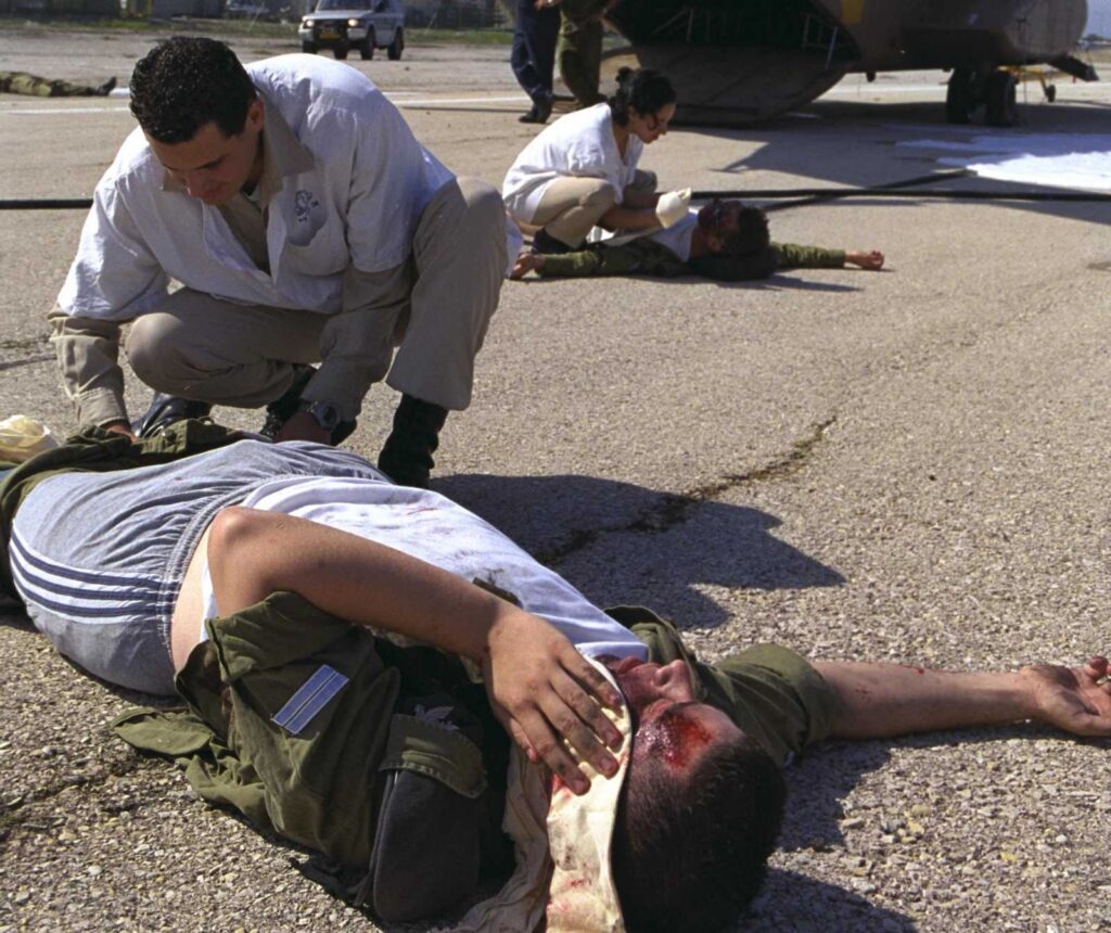 zwei verletzte Menschen liegen auf dem Boden und werden versorgt. Sie bluten, einer hat eine Kopfwundeund hält sich ein weißes Tuch hin