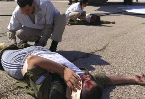 zwei verletzte Menschen liegen auf dem Boden und werden versorgt. Sie bluten, einer hat eine Kopfwundeund hält sich ein weißes Tuch hin