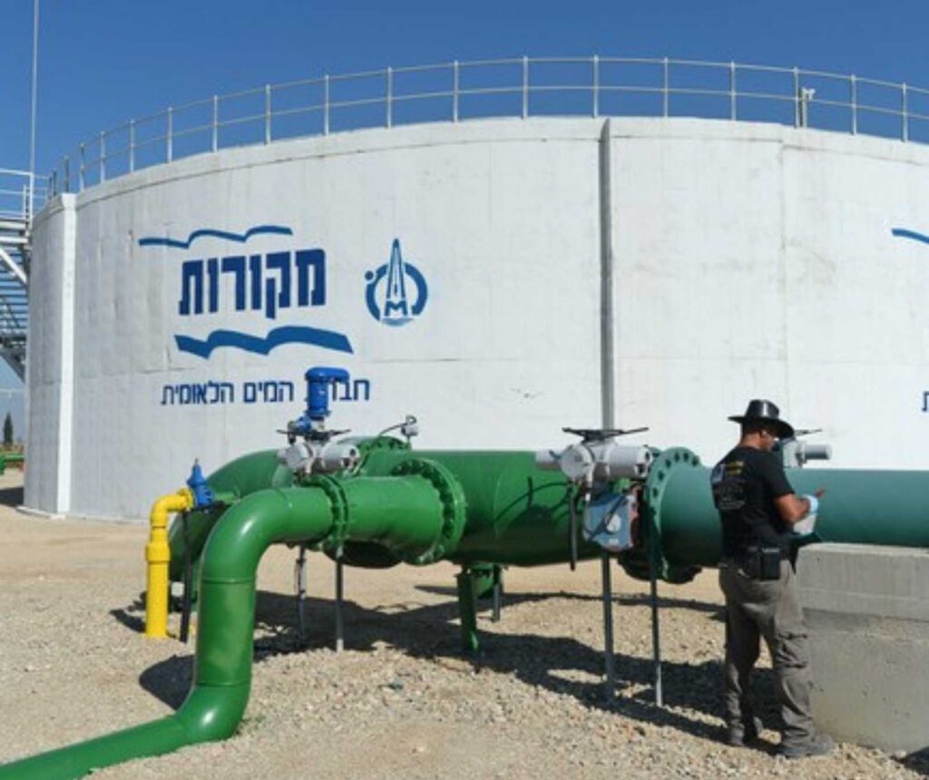 großer runder Wassertank mit angeschlossenen grünen Rohrleitungen. Eine Person steht neben der Anlage