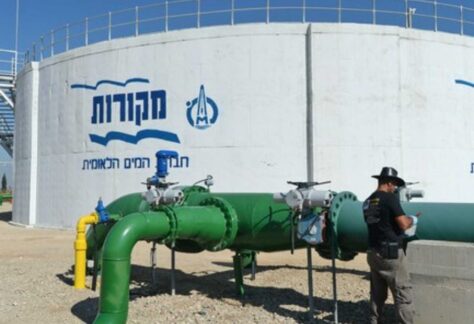 großer runder Wassertank mit angeschlossenen grünen Rohrleitungen. Eine Person steht neben der Anlage