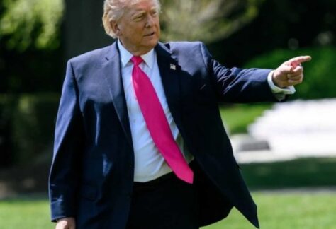 ein Mann mit blauem Anzug und pinkfarbener Krawatte schaut und zeigt mit der linken Hand nach links