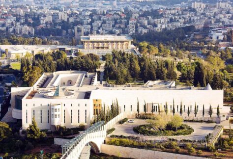 Luftaufnahme einer großen Stadt. Im Vordergrund sieht man ein helles Gebäude