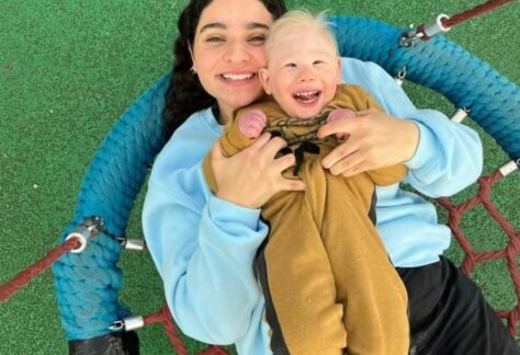 eine Aufnahme von oben auf eine Frau. die ein behindertes Kind auf ihrem Oberkörper liegen hat. Beide lächeln in die Kamera